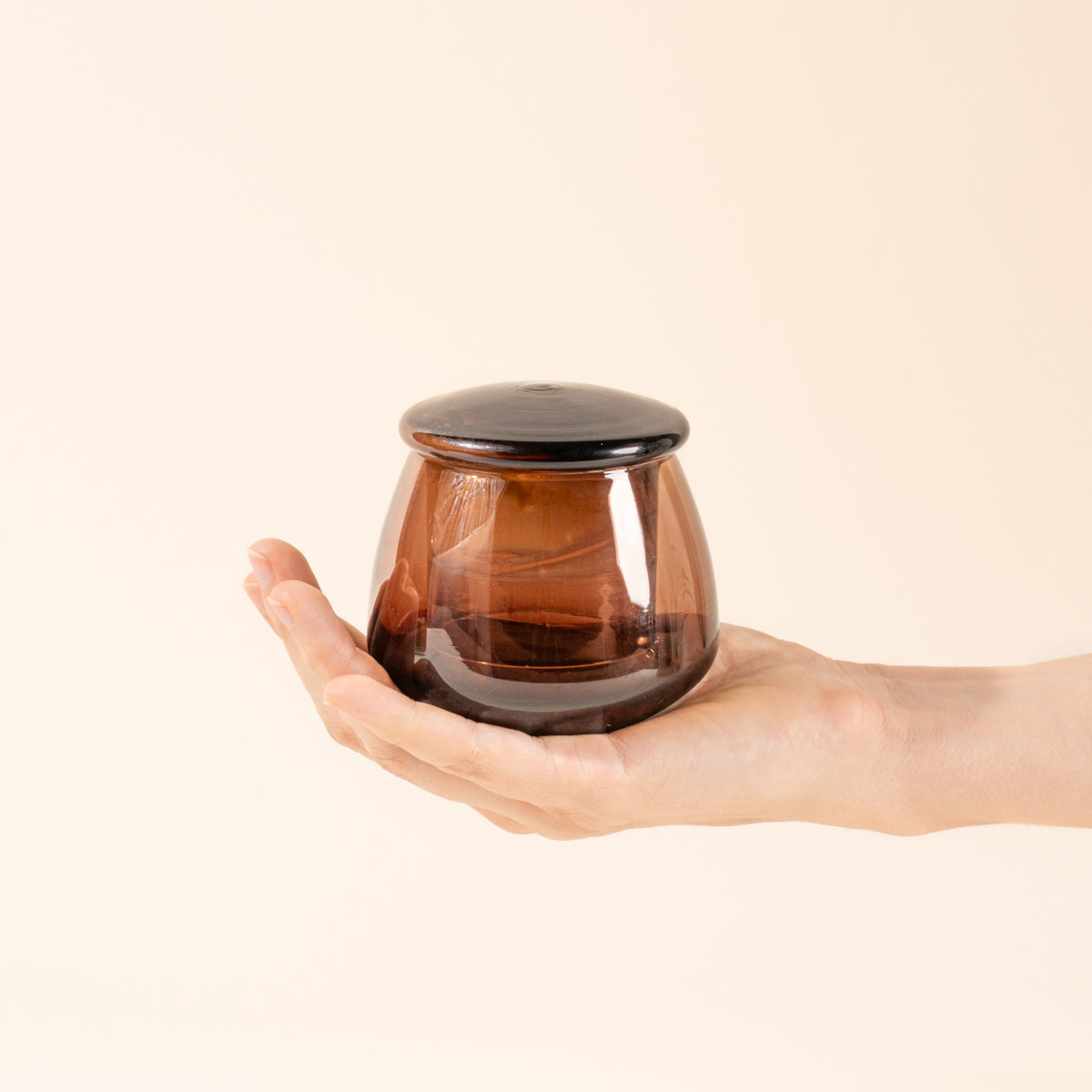 Hand holds a walnut glass butter keeper, filled with butter.