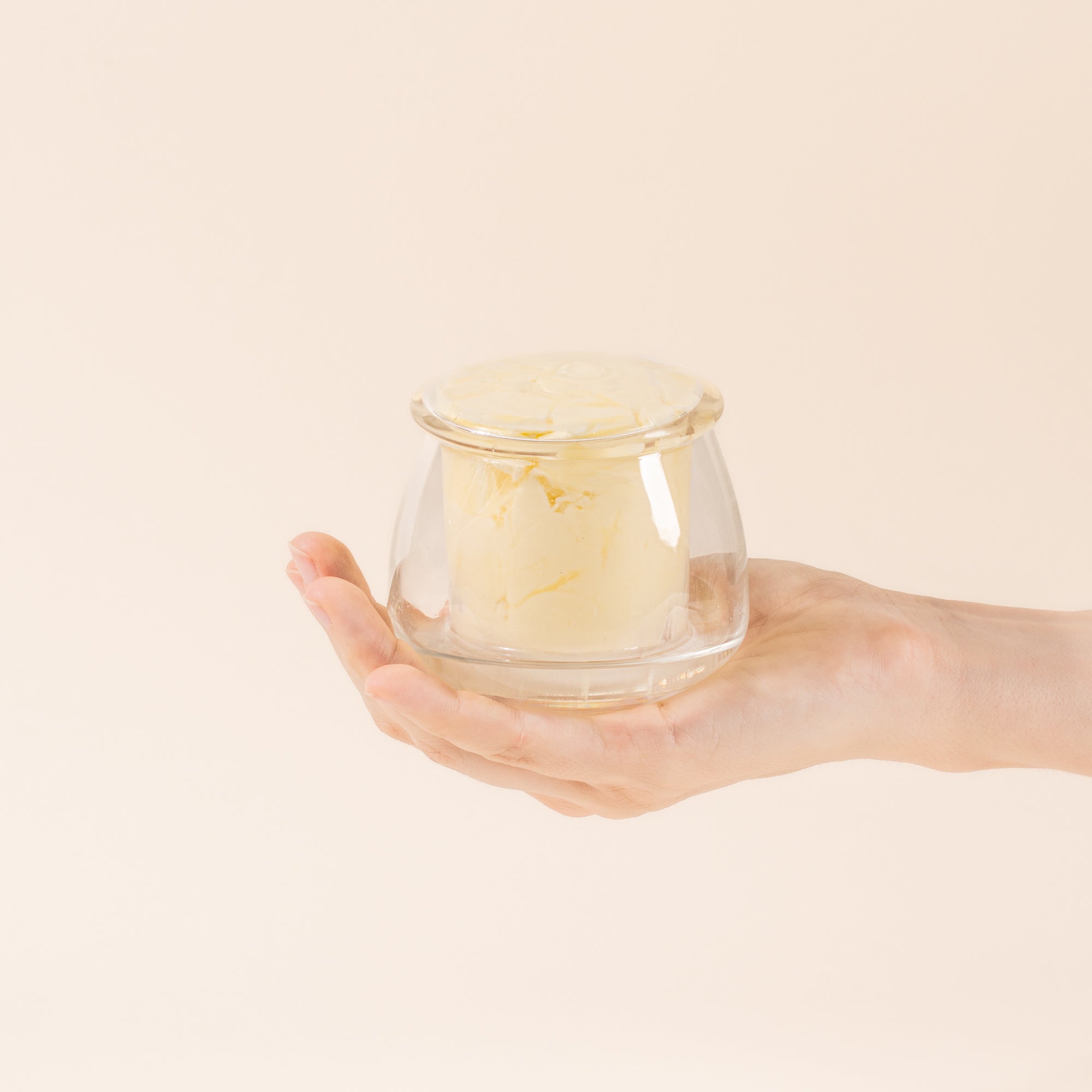 Hand holds a clear glass butter keeper, filled with butter.