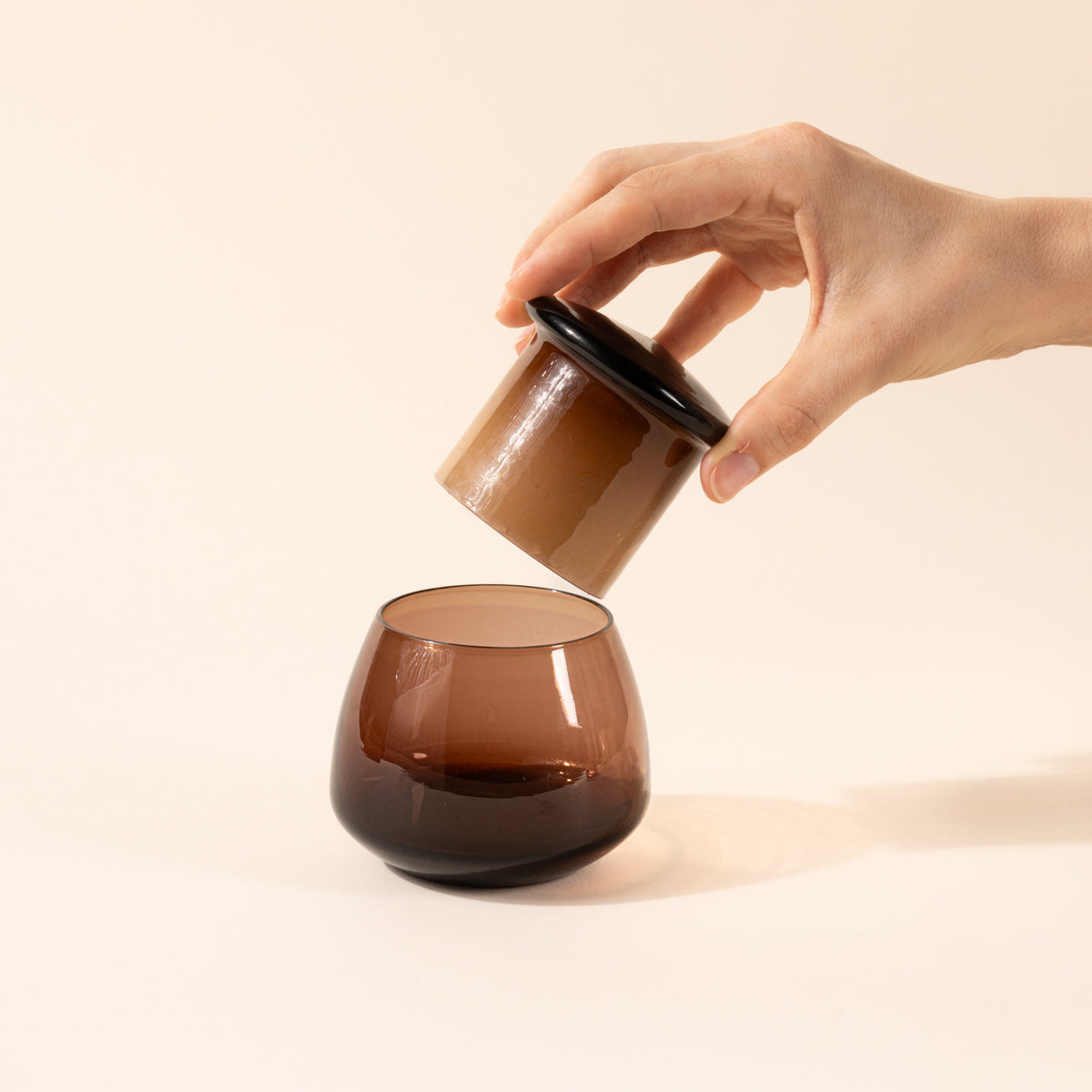 A hand holds the top of the walnut clear butter keeper over the rounded base.