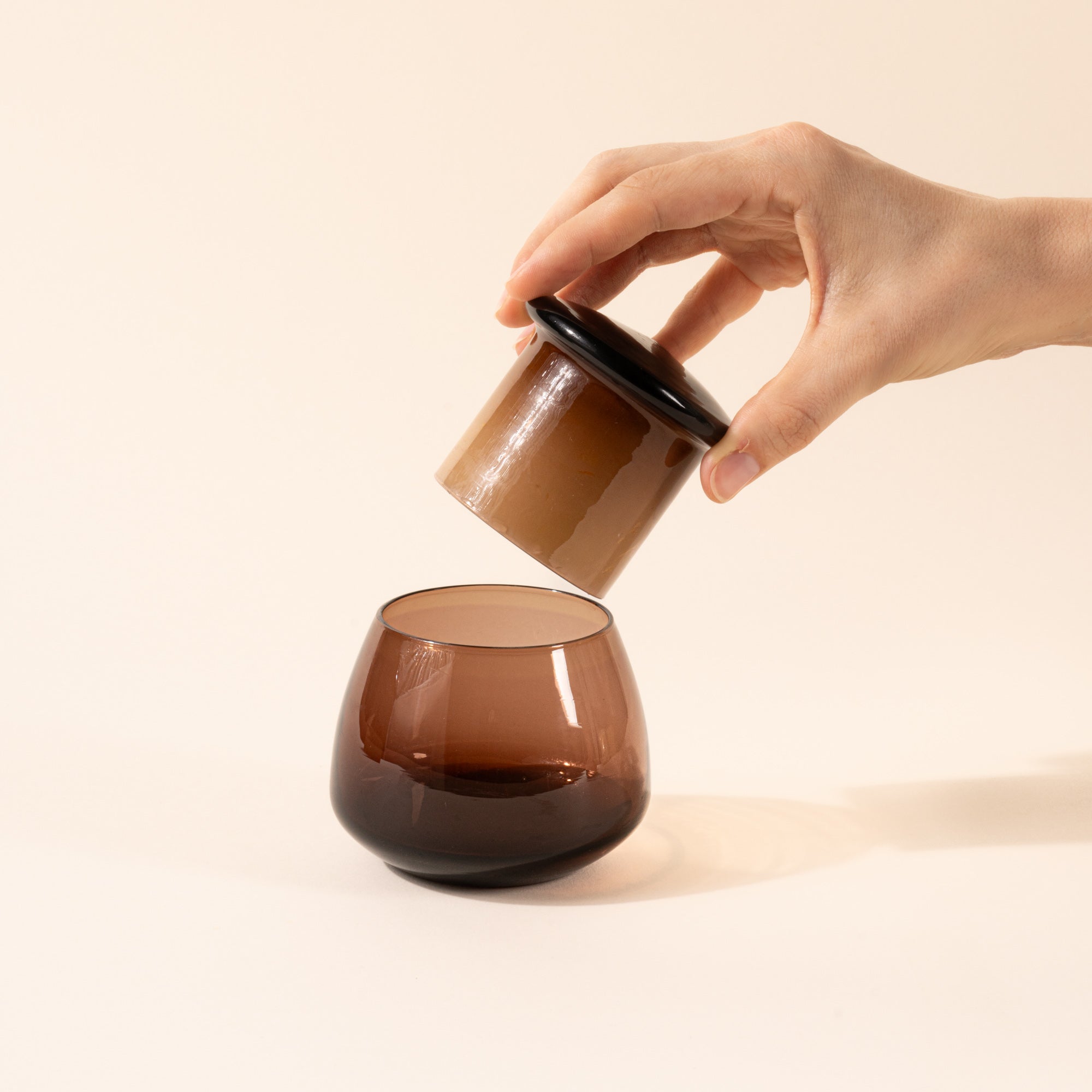 A hand holds the top of the walnut clear butter keeper over the rounded base.