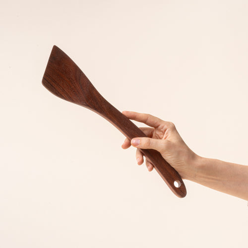 Hand holding a wooden spatula against a beige background