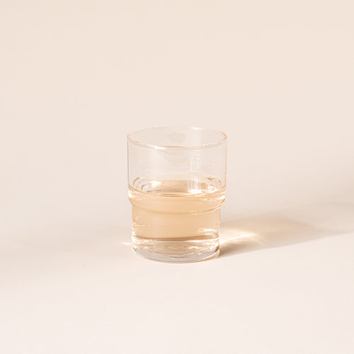 Clear cylindrical glass with a wider top half with a narrower bottom half, filled with a drink.