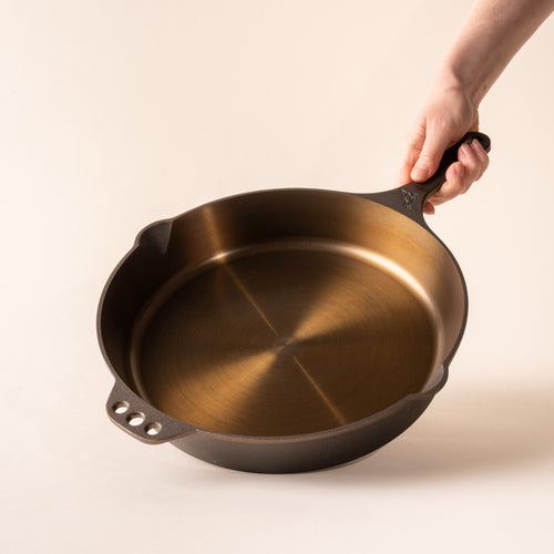 Hand holding the handle of a cast iron skillet titled up