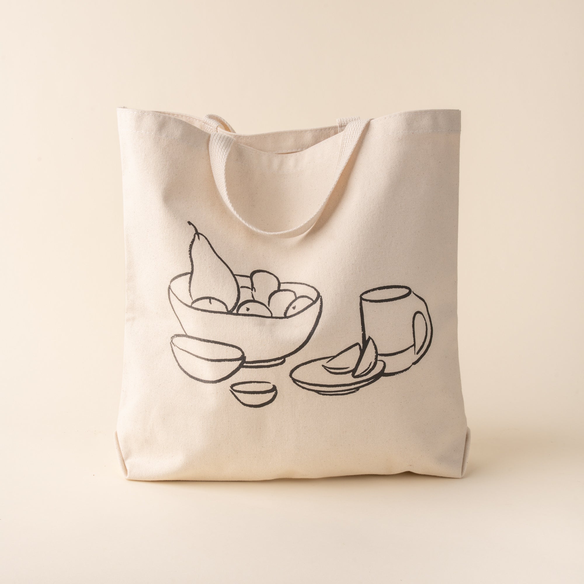 A beige cotton tote bag with a black printed drawing of a bowl and a mug