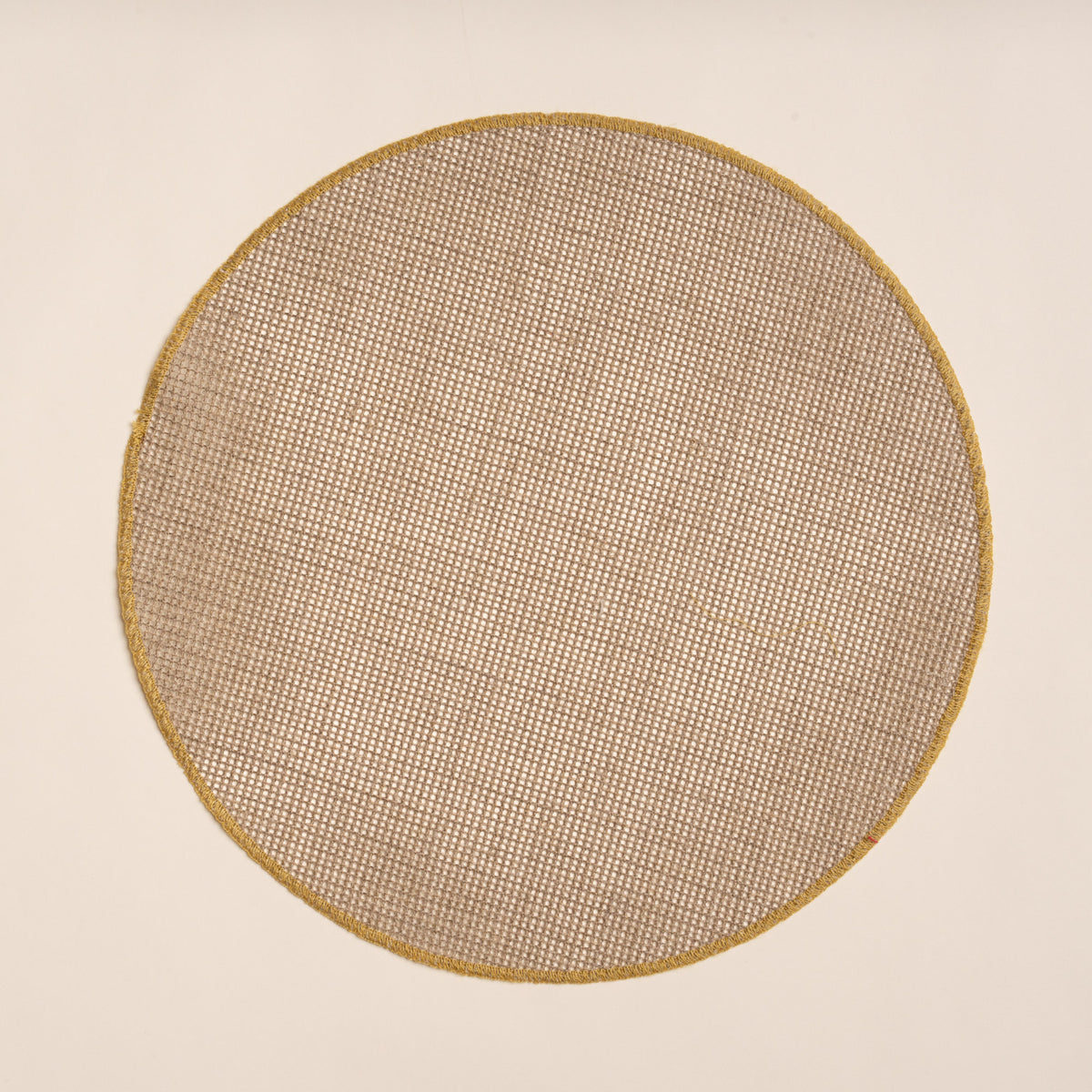 Round woven placemat in a natural color with a sewn ochre rim on a beige background