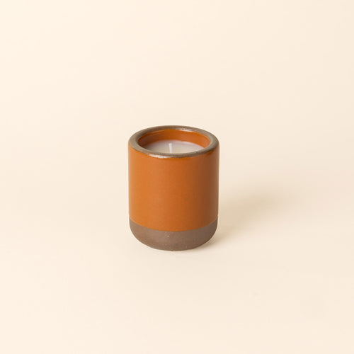Small ceramic vessel in an earthy orange color with candle inside.