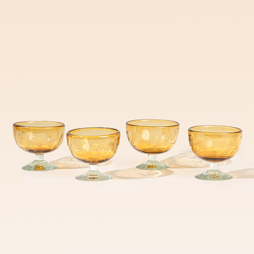 Four amber etched coupe glasses with a pedestal base and delicate botanical pattern, shown on a clean neutral background.