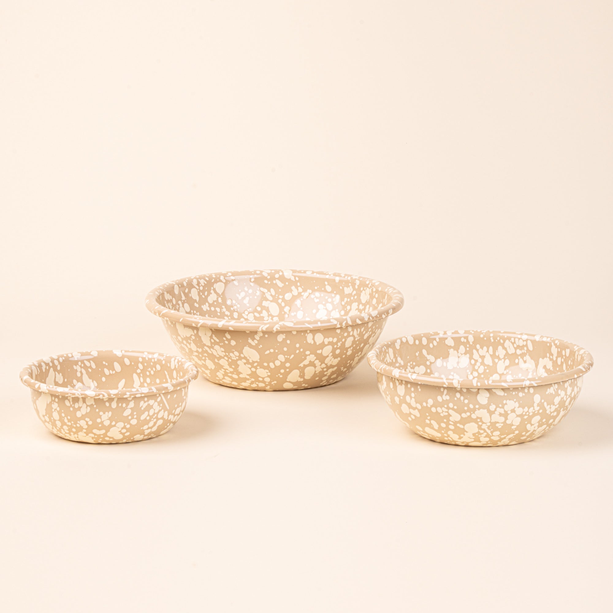 A small, medium, and large enamel bowls in neutral tan color with off-white splatter pattern.