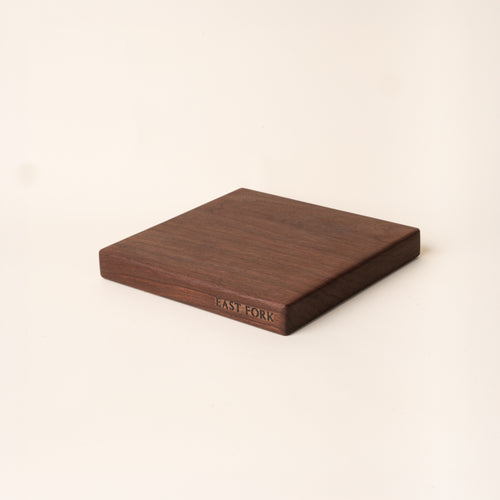 A square walnut cutting board on its side with an engraving on the edge that reads 'East Fork'