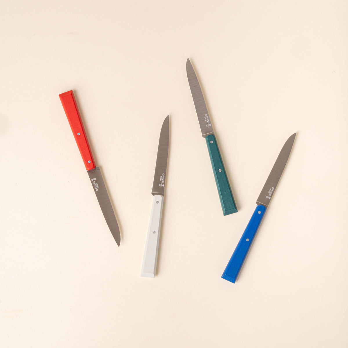 A set of four Opinel table or steak knives with slim stainless-steel blades and colorful handles in red, white, green, and blue.