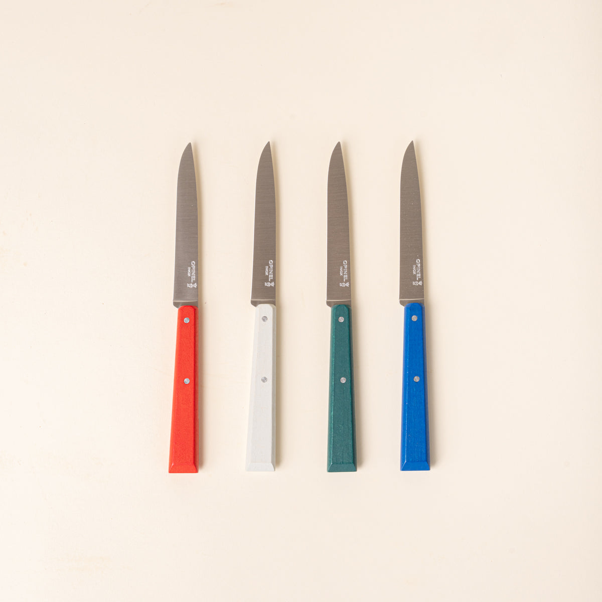 A set of four Opinel table or steak knives with slim stainless-steel blades and colorful handles in red, white, green, and blue.