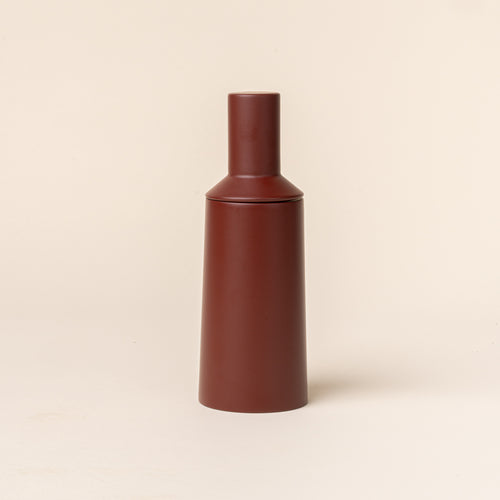 A tall cylindrical sculptural salt and pepper grinder in dark red on a light background.