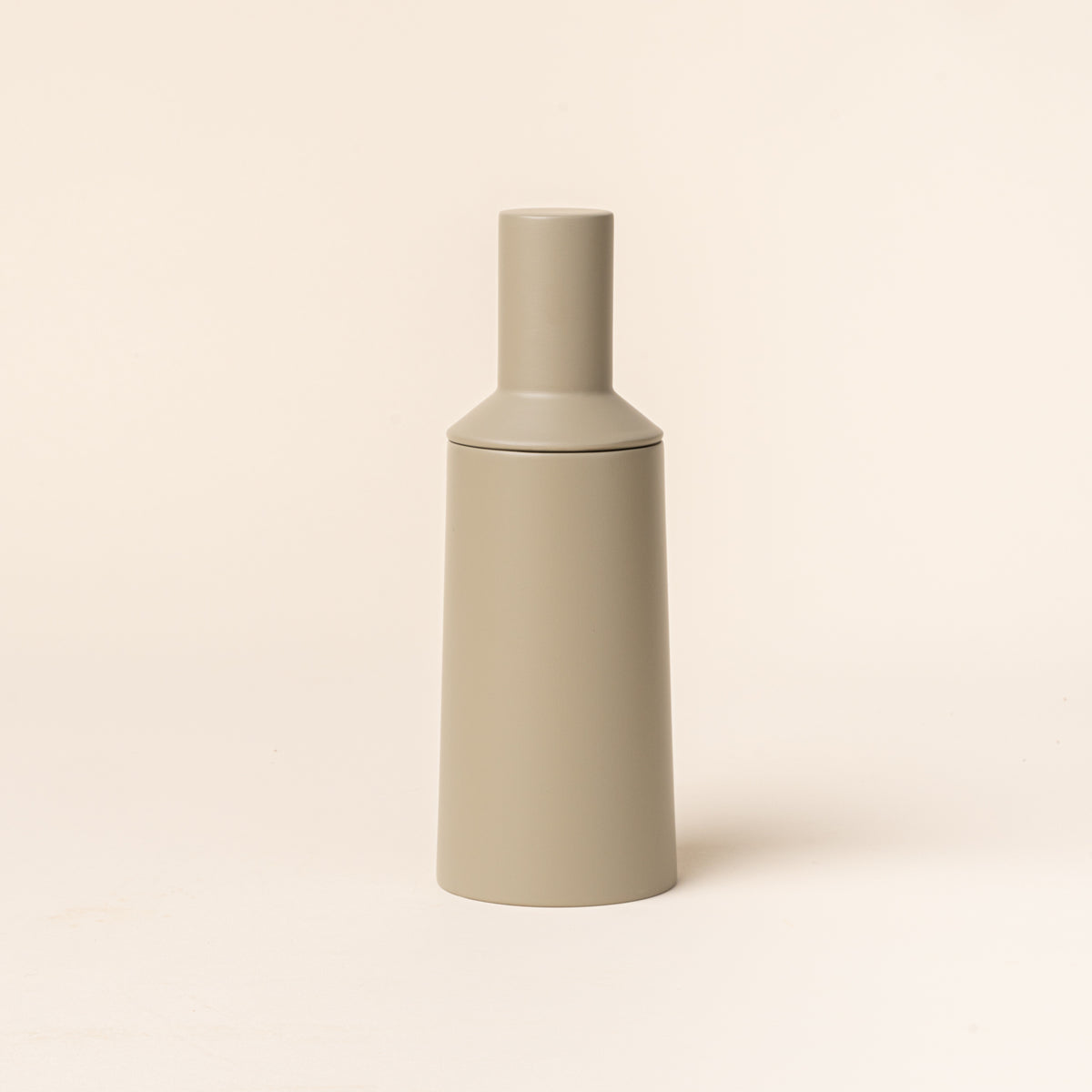 A tall cylindrical sculptural salt and pepper grinder in a muted light green on a light background.
