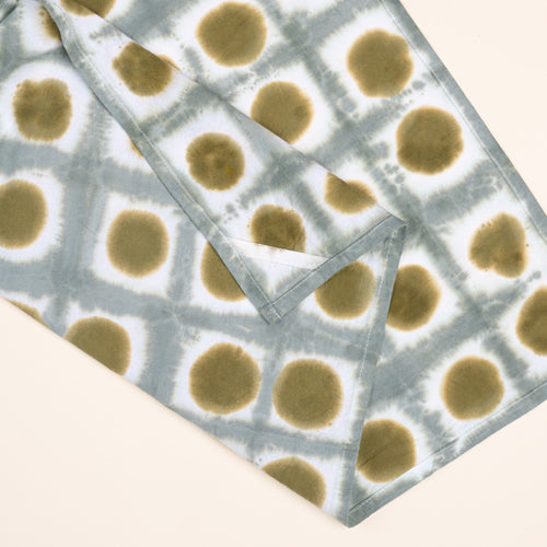 A closeup of a tie-dye tea towel in a green colorway with a hanging corner tag