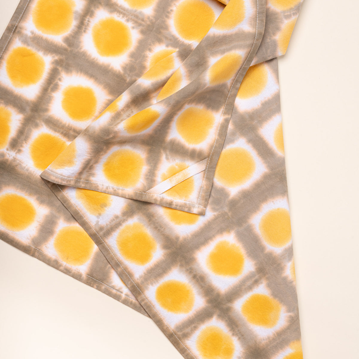 A closeup of a tie-dye tea towel in a yellow colorway with a hanging corner tag