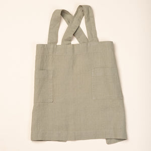 Front of a linen child aprons in light sage green with front pockets and shoulder straps.