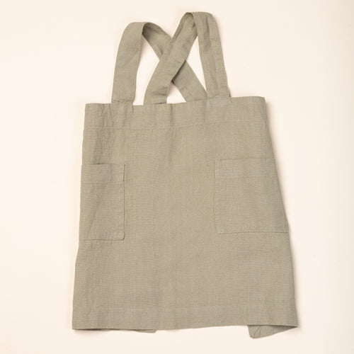 Front of a linen child aprons in light sage green with front pockets and shoulder straps.