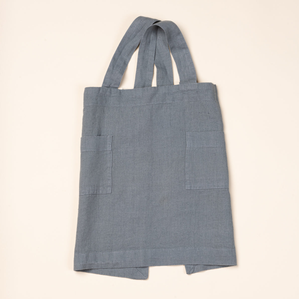 Front of a linen child aprons in blue with front pockets and shoulder straps.