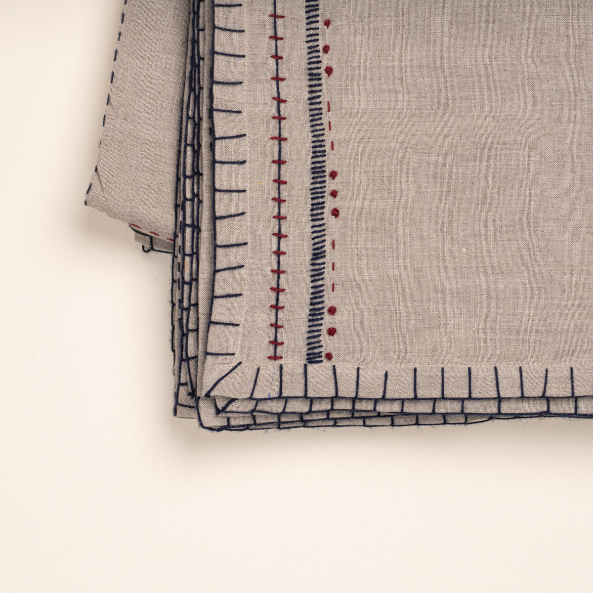 Closeup of folded natural linen tablecloth with hand-stitched navy and rust detailing and a decorative geometric border.