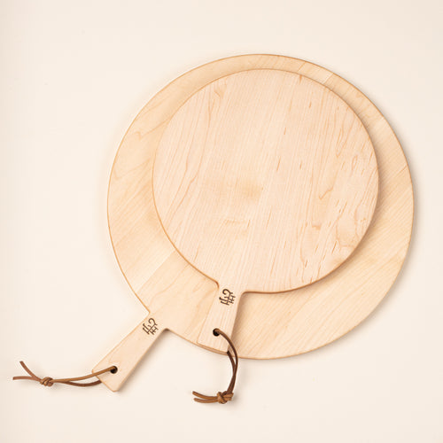 A small and large round maple serving boards in different sizes, each with a short handle and leather hanging loop.