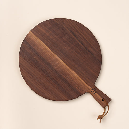 A small round walnut serving board with a short handle and leather hanging loop.