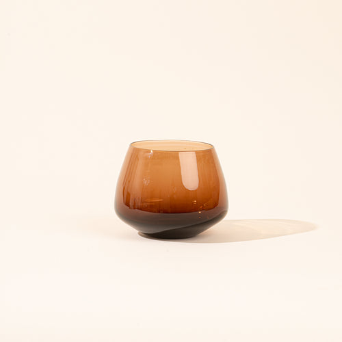 A rounded smoky amber colored glass against a light neutral background.