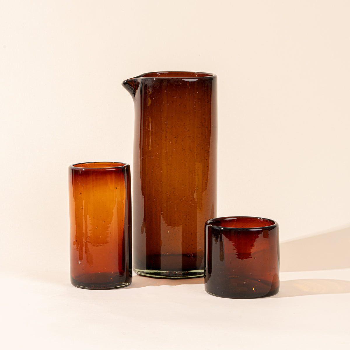 A tall tumbler, large pitcher, and short tumbler, of dark amber glassware.