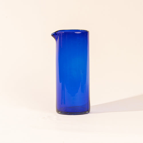 A cobalt blue tall transparent glass pitcher with small spout at the top