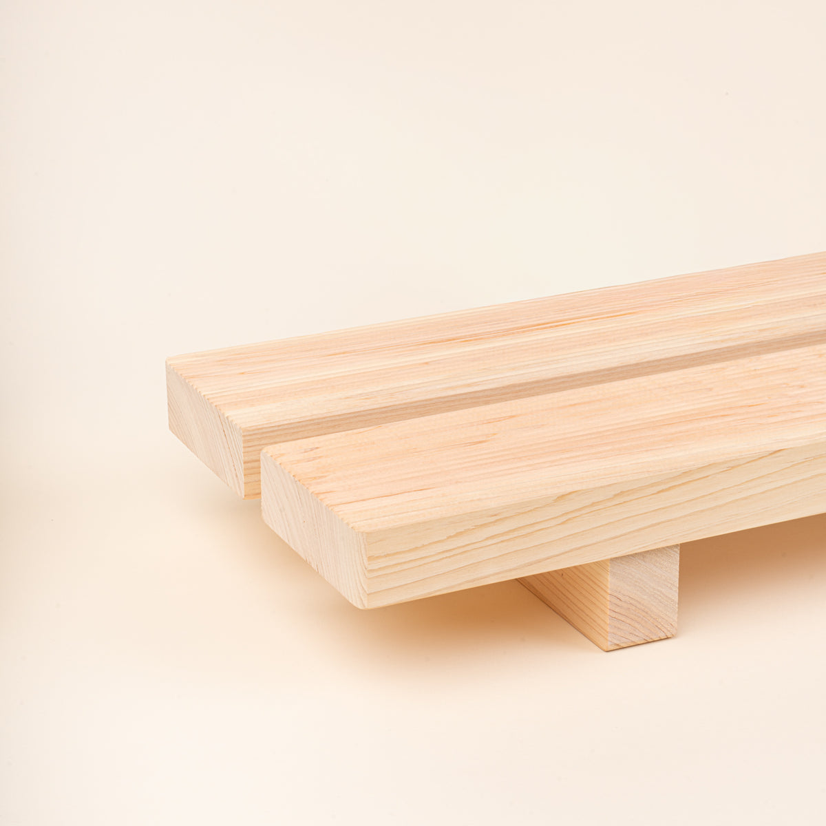 Closeup of a long, low unfinished-wood bath tray made from two parallel planks, with simple block feet. 