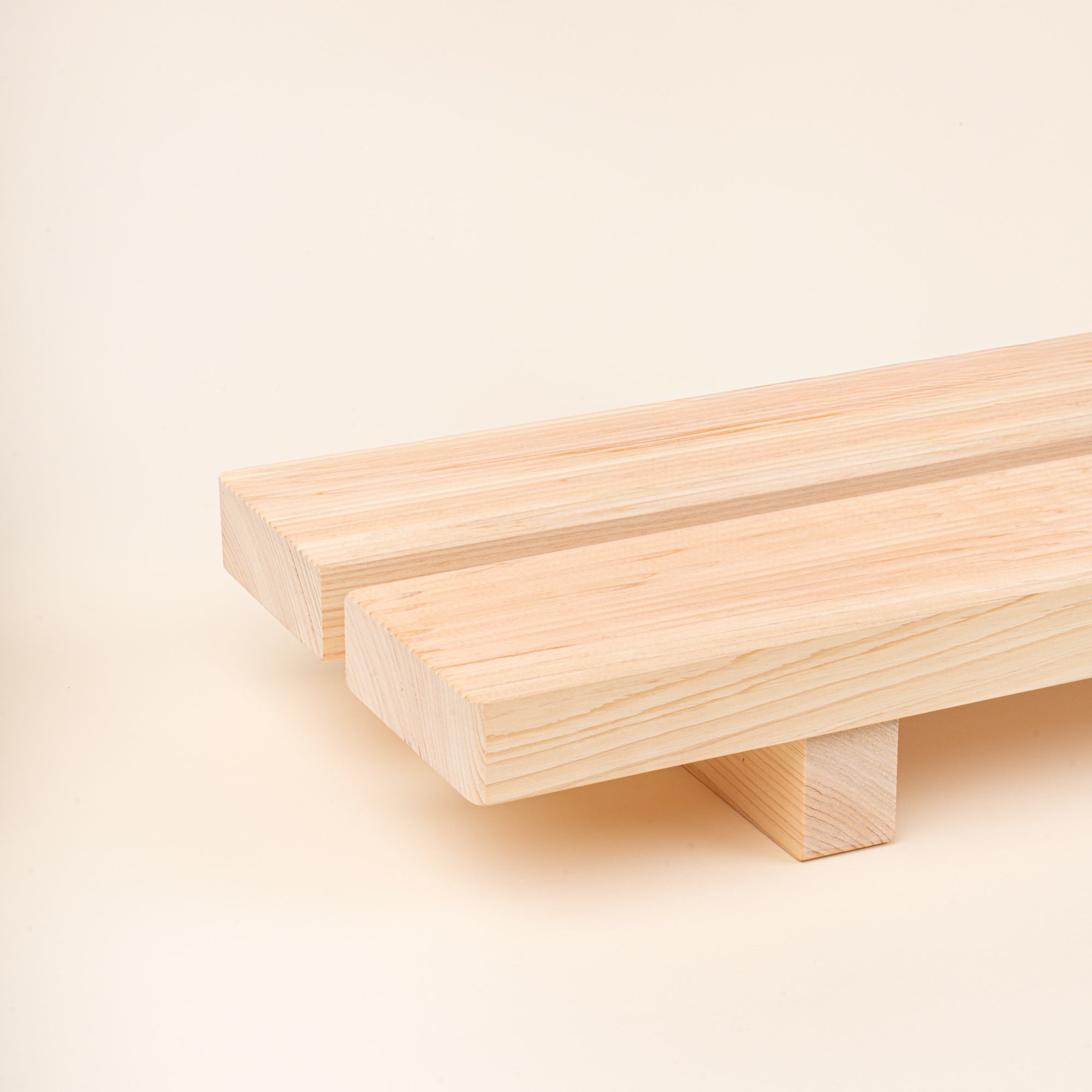 Closeup of a long, low unfinished-wood bath tray made from two parallel planks, with simple block feet. 