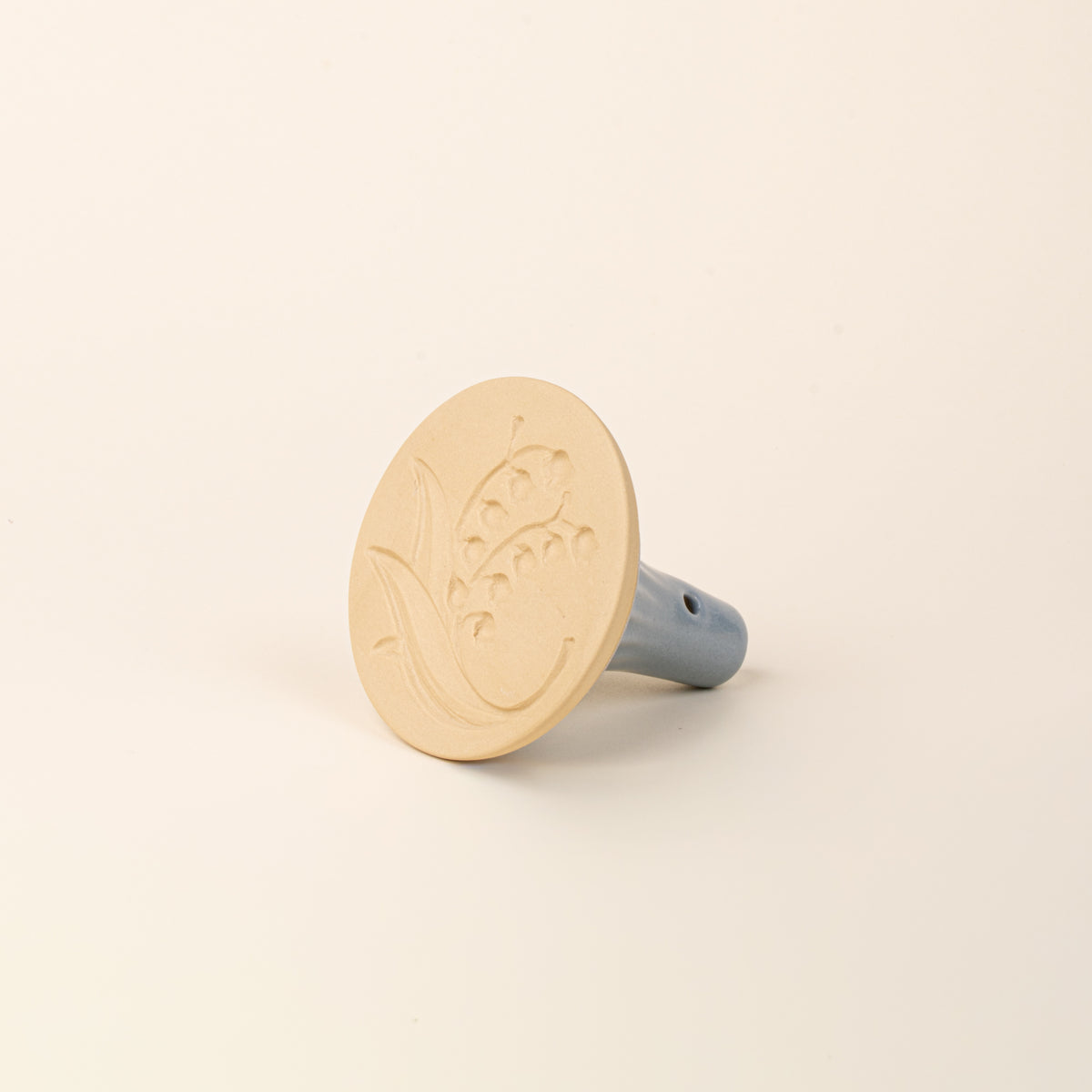 Hand holding a cookie stamp showing the bottom featuring the design of a lily of the valley
