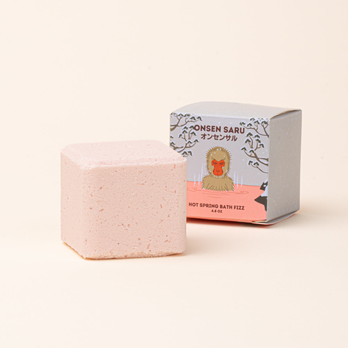Onsen Saru Hot Spring Bath Fizz, a pale pink bath cube presented beside its illustrated packaging.