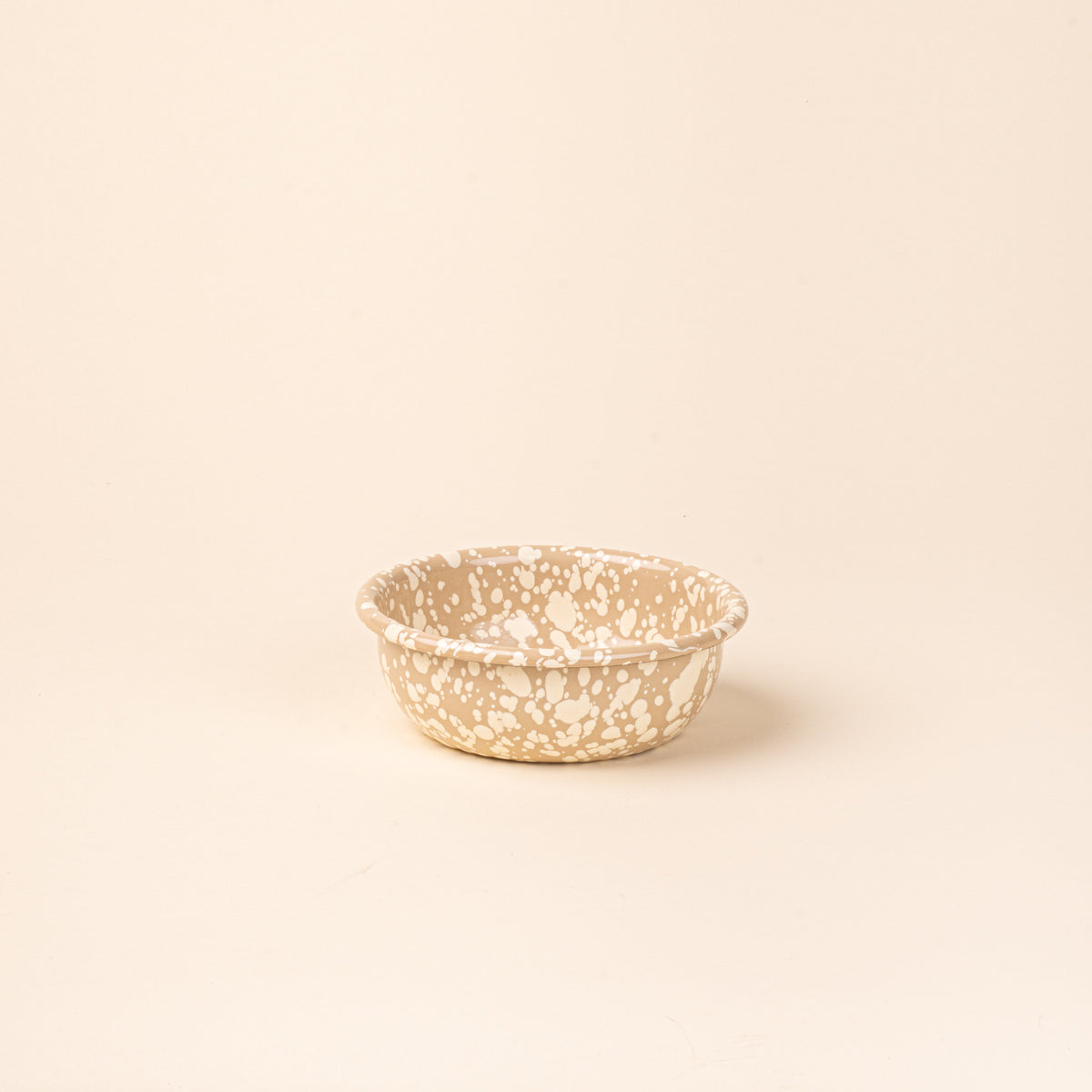 A small enamel bowl in neutral tan color with off-white splatter pattern.