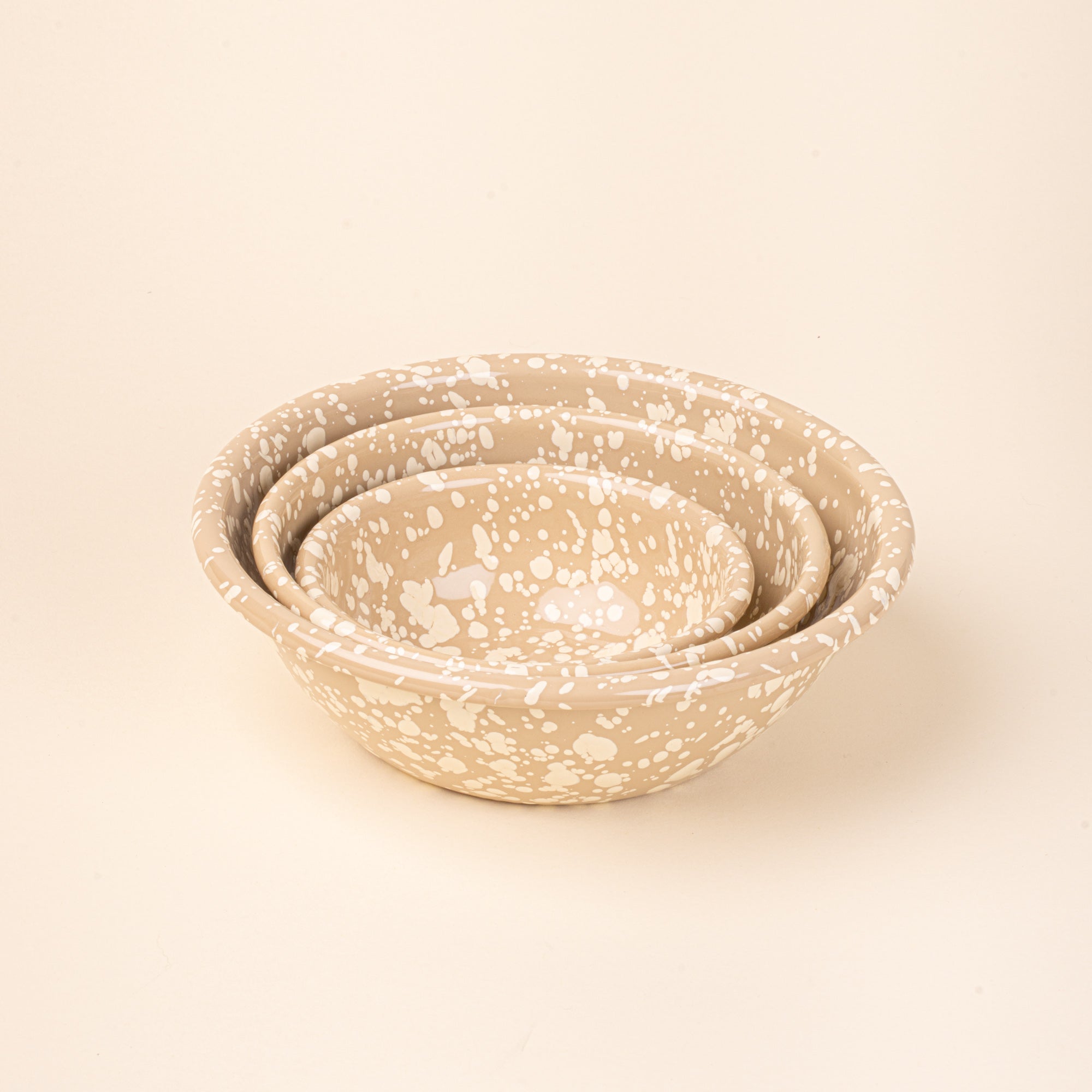 A nesting trio of a enamel bowls in neutral tan color with off-white splatter pattern.
