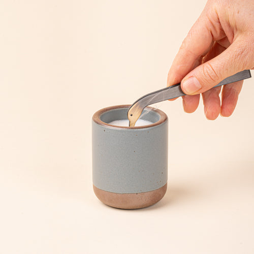 A hand holds a simple steel clamp candle snuffer with a tip that is a duck head silhouette with eyes, above a candle.