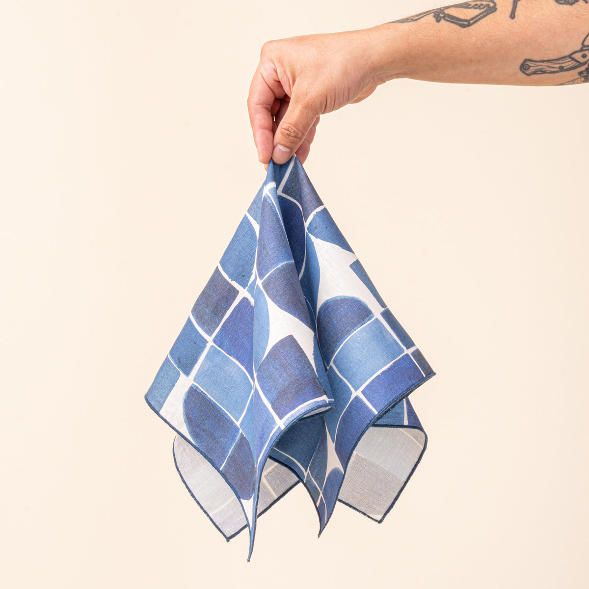A hand holds a blue-and-white cloth napkin featuring a bold geometric pattern of squares, curves, and intersecting lines.