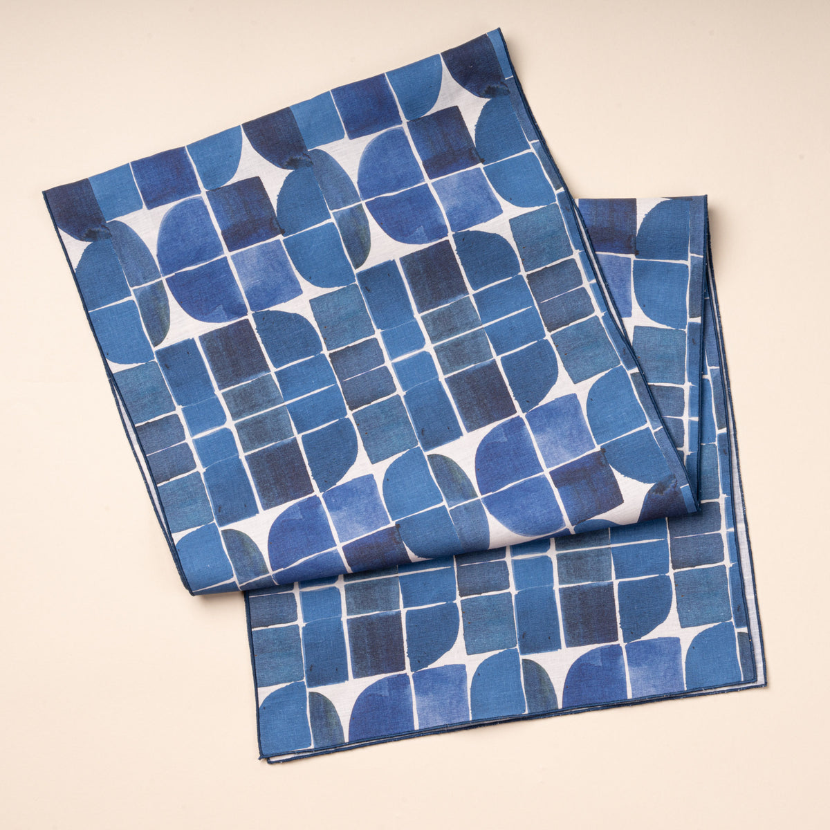 A blue-and-white cloth table runner featuring a bold geometric pattern of squares, curves, and intersecting lines.