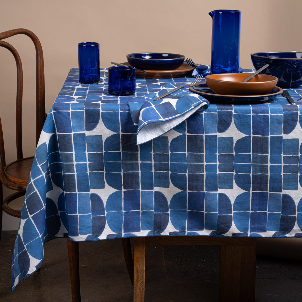 Blue-and-white geometric tablecloth and matching napkins styled with cobalt glassware and warm ceramic dinnerware.