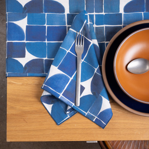 Blue geometric napkin and tablecloth paired with warm orange and deep navy dinnerware on a wood table.