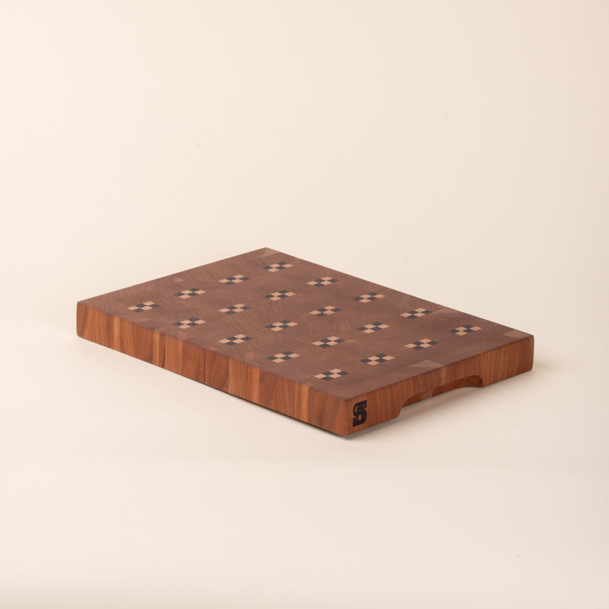 Rectangular wooden cutting board with repeating geometric inlay pattern on a light background.