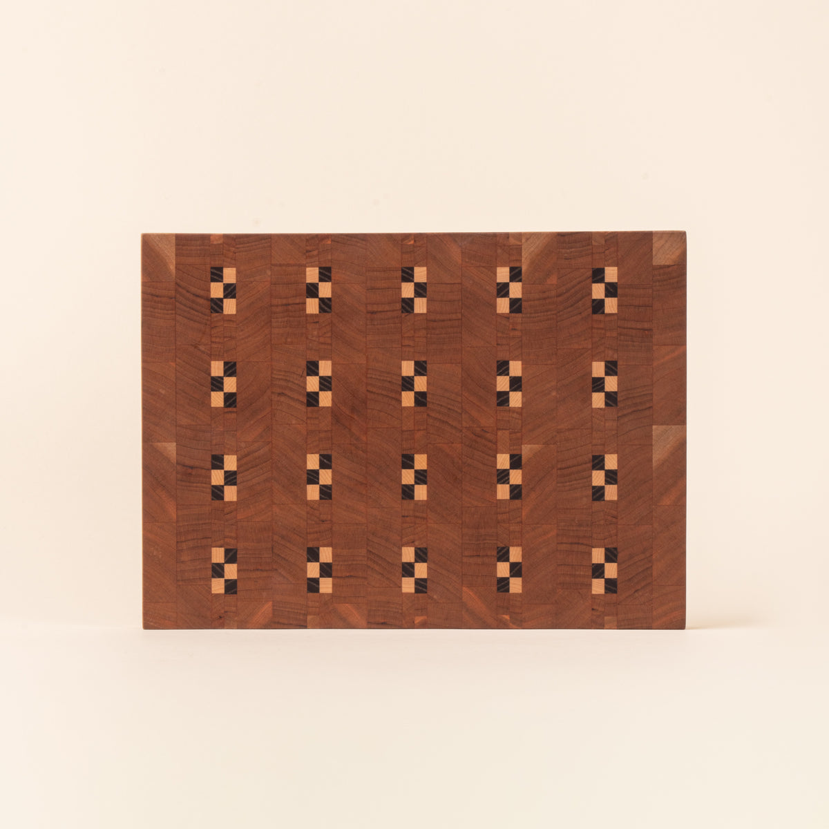 Rectangular wooden cutting board with repeating geometric inlay pattern on a light background.