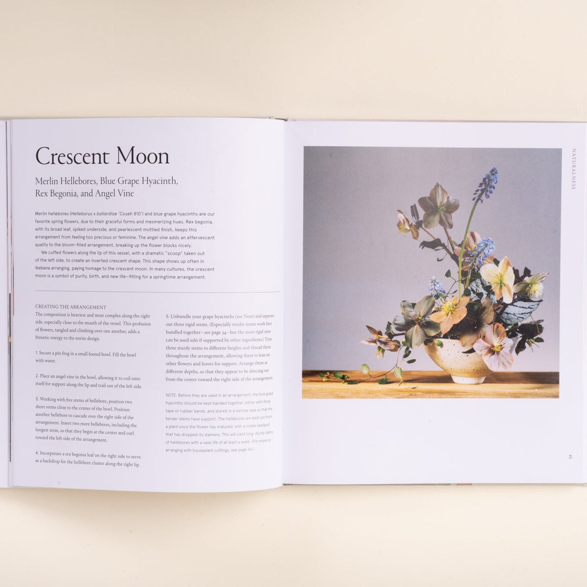 An book, Ikebana Unbound, laid flat on a light beige surface, showing a page titled 'Crescent Moon' with text on the left and a still life floral photograph on the right.