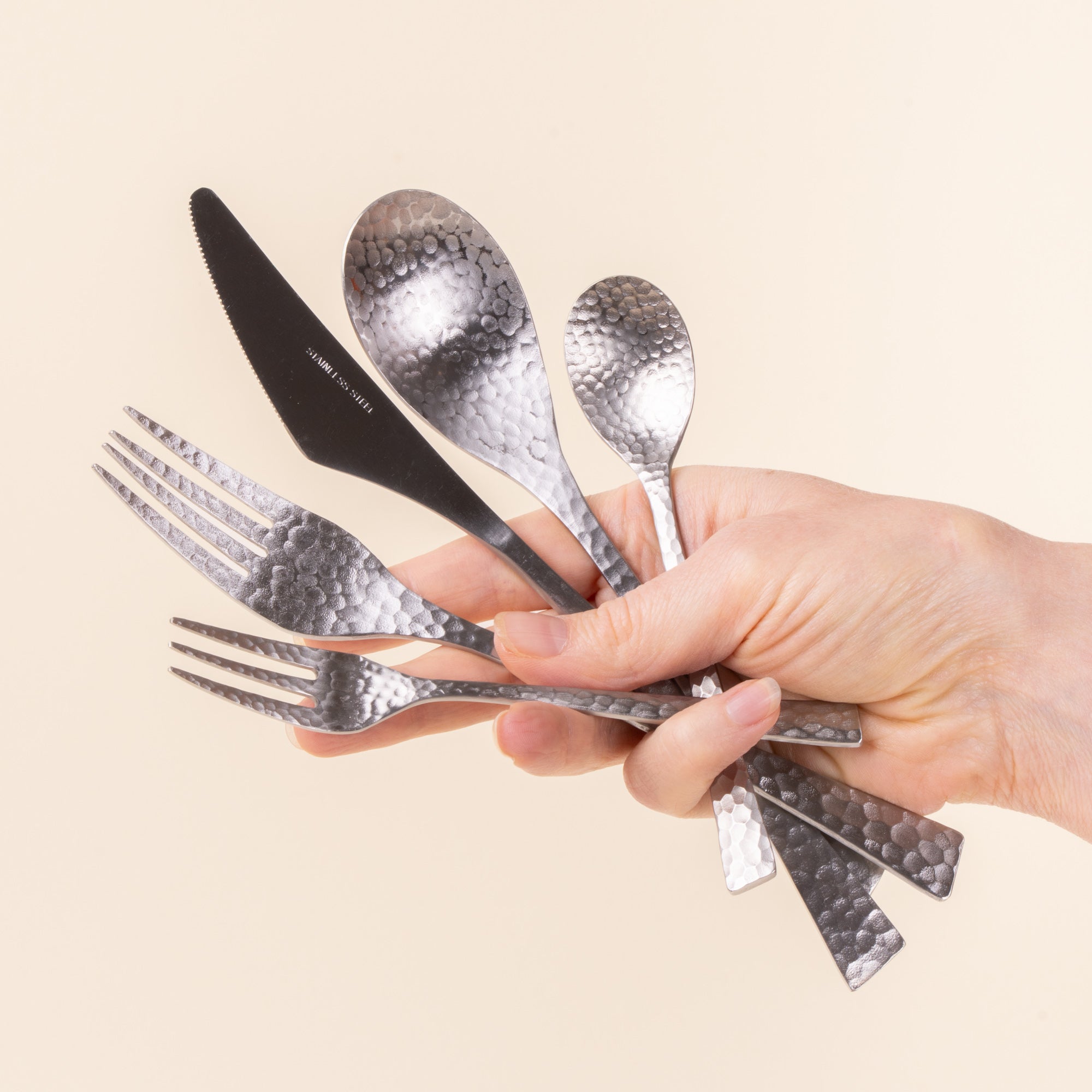 A hand holds a hammered stainless steel 5 piece flatware