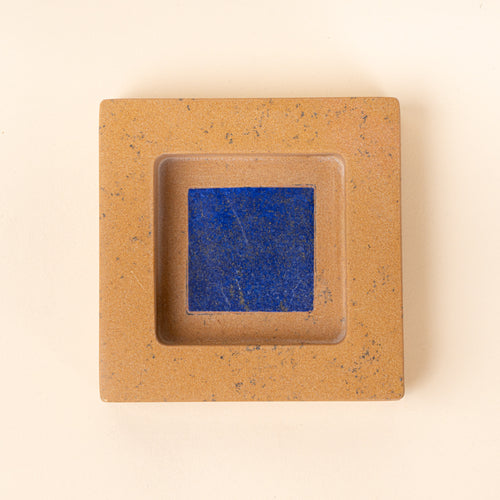 Overhead view of a square tan speckled jewelry dish with a recessed center and blue interior.