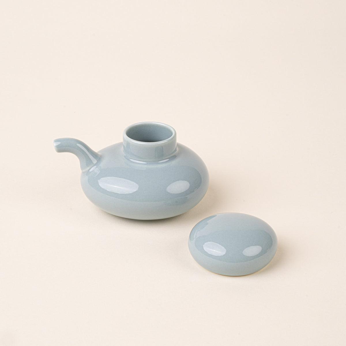 A pale blue glazed ceramic soy sauce pot with a low, rounded body, short pouring spout, and domed lid to the side.
