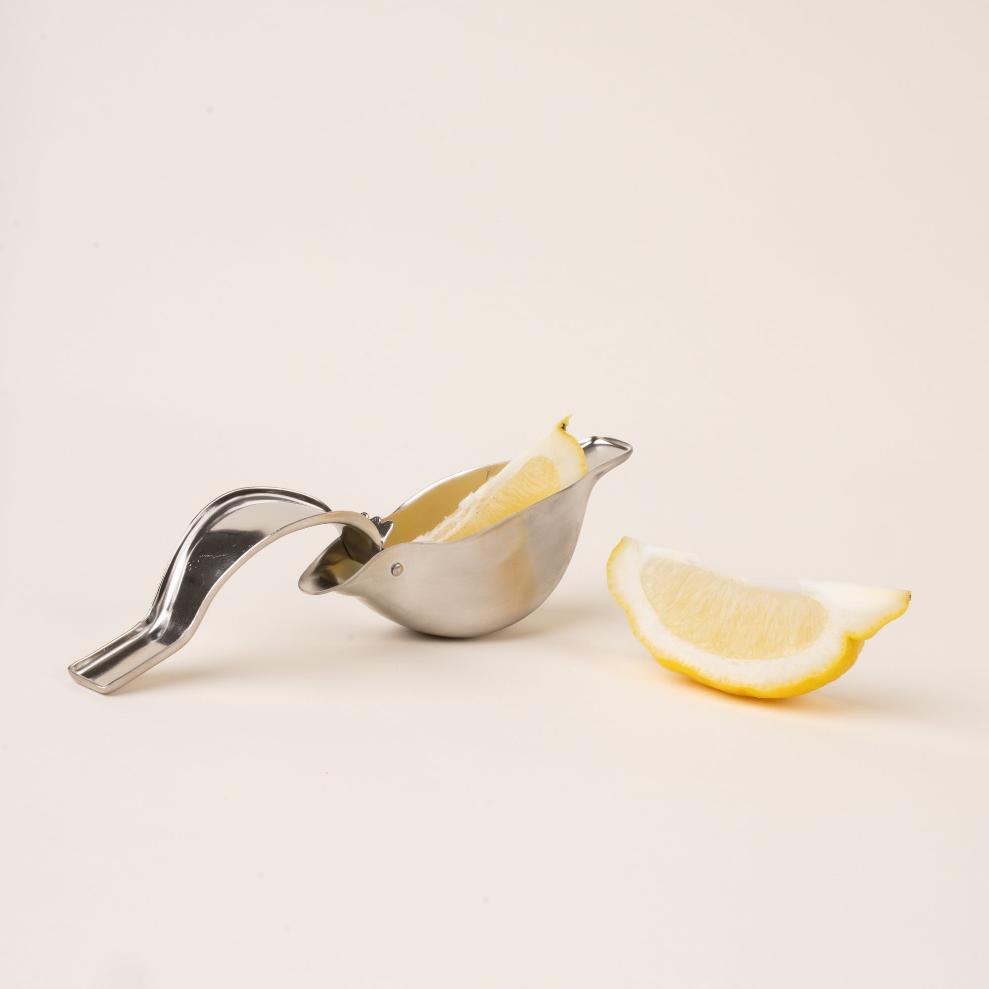 An open sculptural stainless-steel lemon squeezer with a bird-like silhouette, with lemon slices.