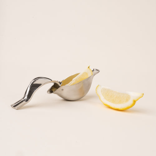 An open sculptural stainless-steel lemon squeezer with a bird-like silhouette, with lemon slices.