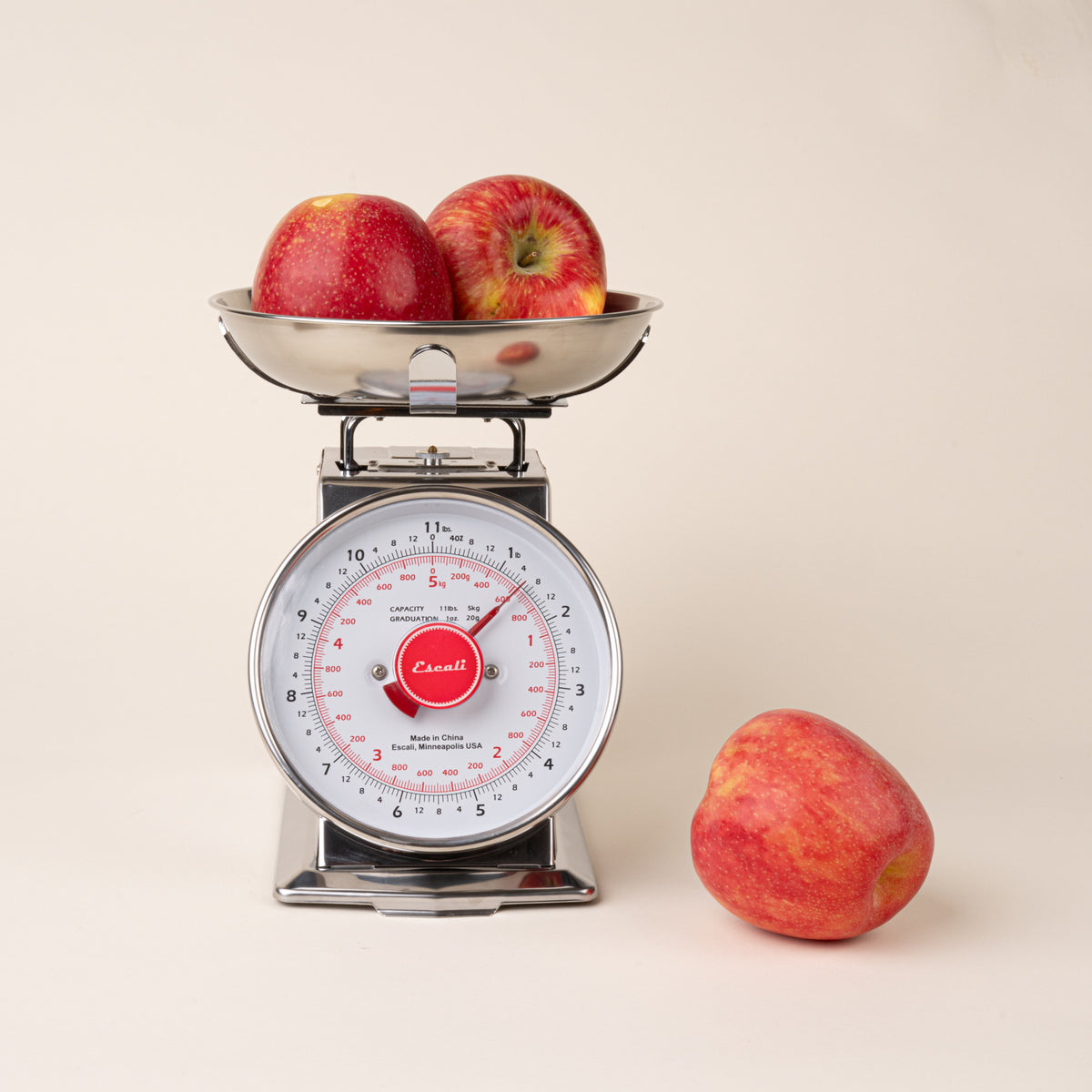 Stainless steel vintage kitchen scale with two red apples in the weighing bowl and one apple beside it.