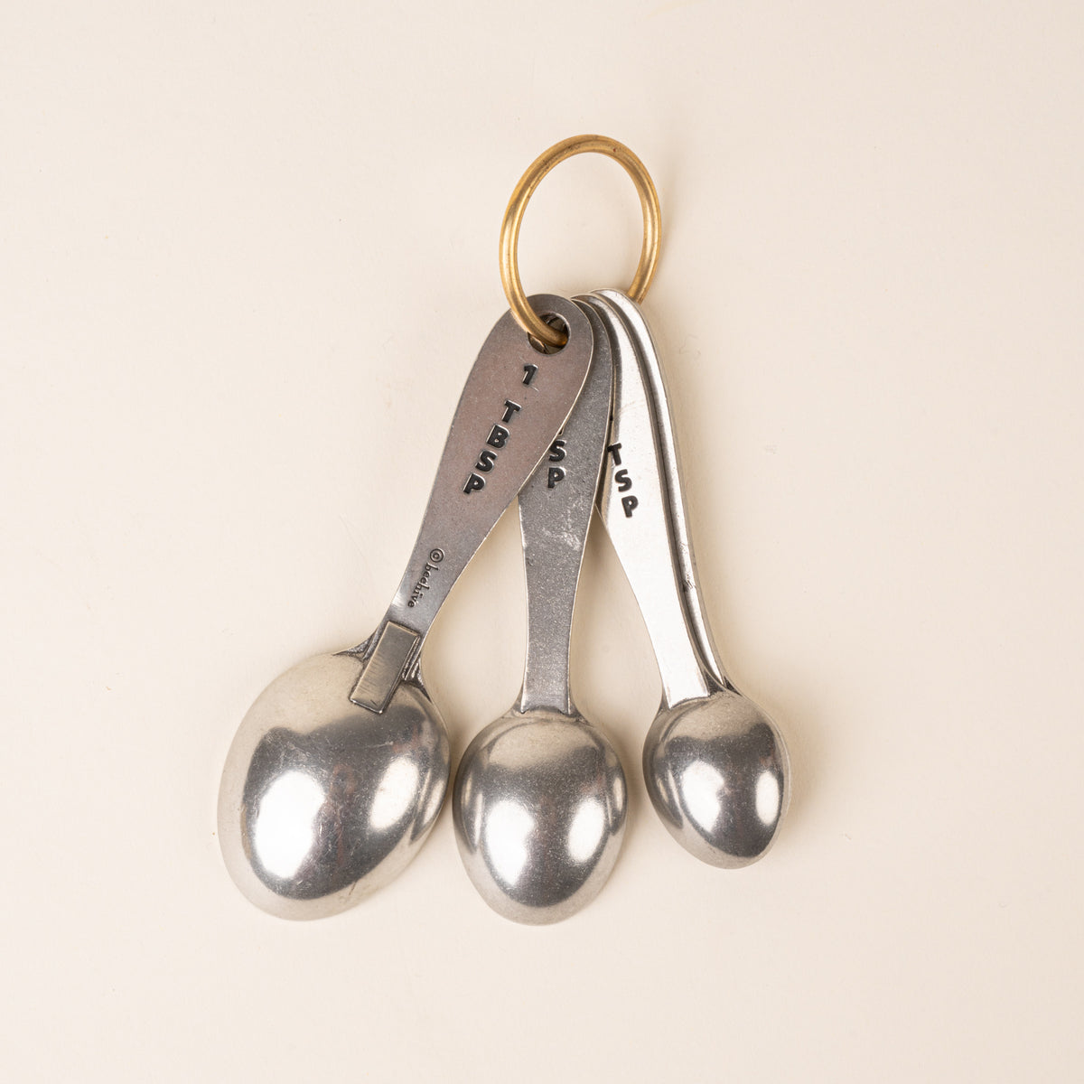 The back of four pewter measuring spoons on a brass ring, displaying the measurement.