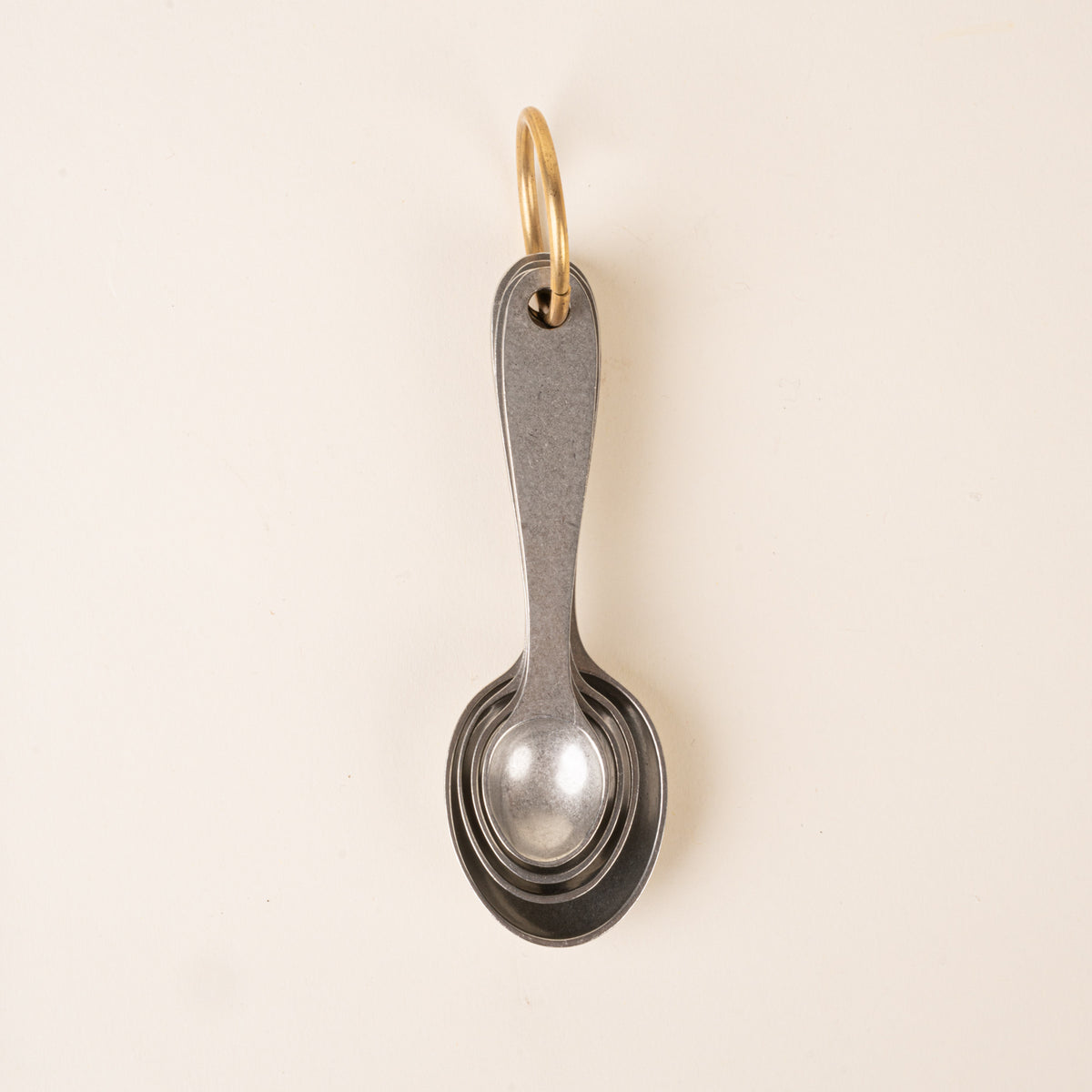 Four pewter measuring spoons on a brass ring, nested together.
